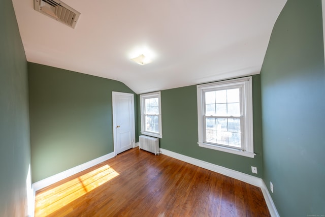 empty room featuring hardwood / wood-style flooring, radiator, and lofted ceiling