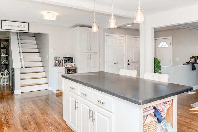 kitchen with white cabinetry, decorative light fixtures, a kitchen island, and light hardwood / wood-style flooring