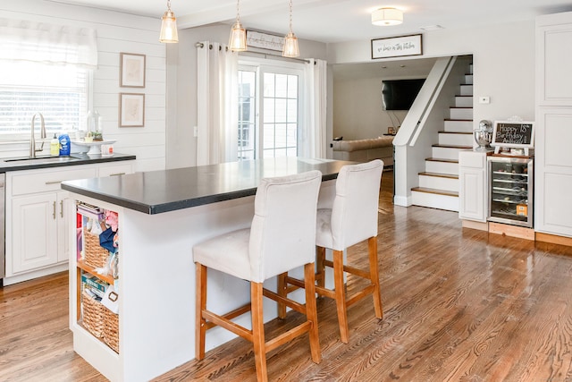 kitchen featuring sink, a breakfast bar area, white cabinetry, a kitchen island, and beverage cooler