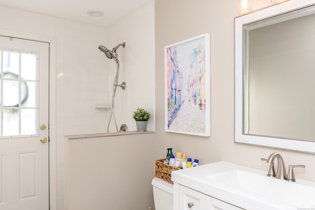 bathroom with tiled shower, vanity, and toilet