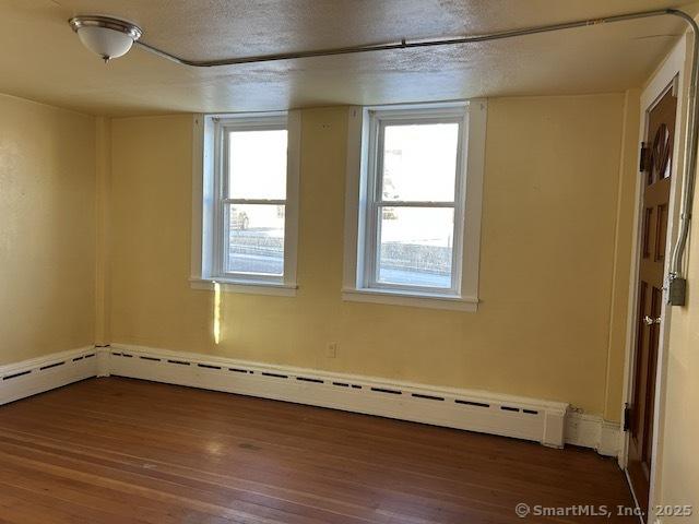 unfurnished room with dark hardwood / wood-style floors, a textured ceiling, and a baseboard heating unit