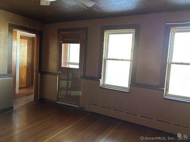 unfurnished room featuring baseboard heating, a healthy amount of sunlight, and dark hardwood / wood-style floors