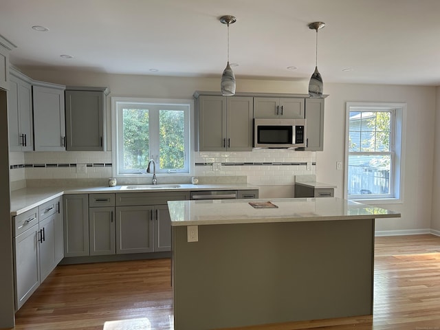 kitchen with light stone countertops, gray cabinetry, sink, pendant lighting, and stainless steel appliances