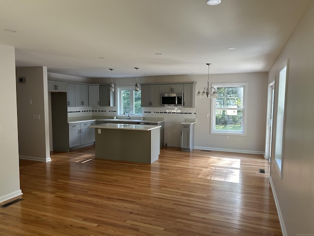 kitchen with hanging light fixtures, backsplash, gray cabinetry, a wealth of natural light, and a center island