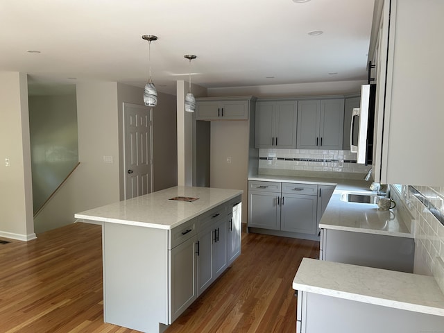 kitchen featuring wood-type flooring, gray cabinetry, sink, a kitchen island, and decorative light fixtures