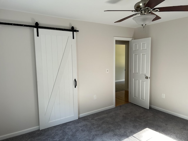 unfurnished bedroom with ceiling fan, dark carpet, and a barn door