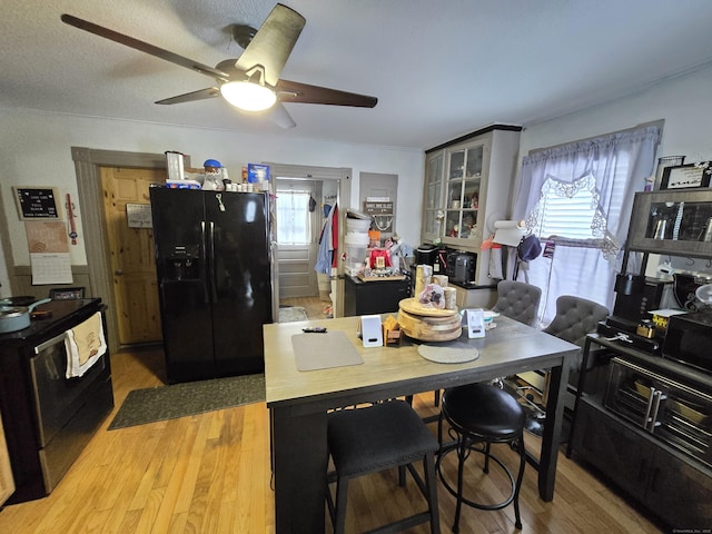 kitchen featuring stainless steel range with electric cooktop, black fridge with ice dispenser, a healthy amount of sunlight, and wood-type flooring