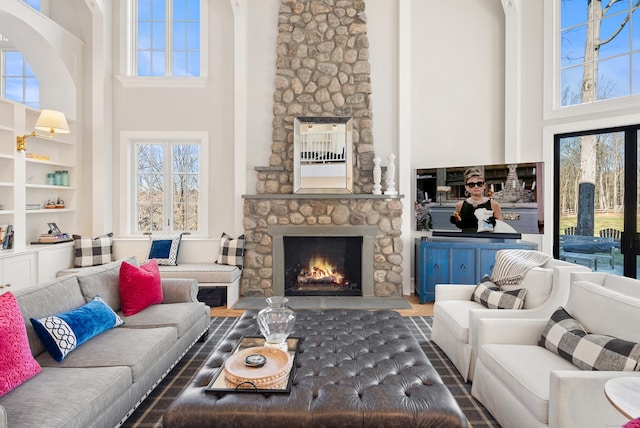 living room with a high ceiling, built in features, and a stone fireplace