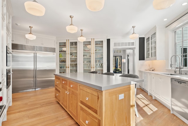 kitchen with built in fridge, dishwashing machine, a kitchen island, white cabinets, and sink