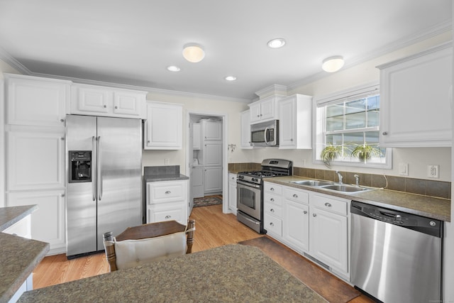 kitchen with ornamental molding, stainless steel appliances, sink, hardwood / wood-style floors, and white cabinetry