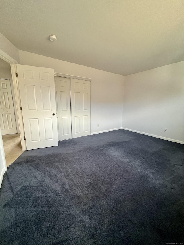 unfurnished bedroom with dark colored carpet and a closet