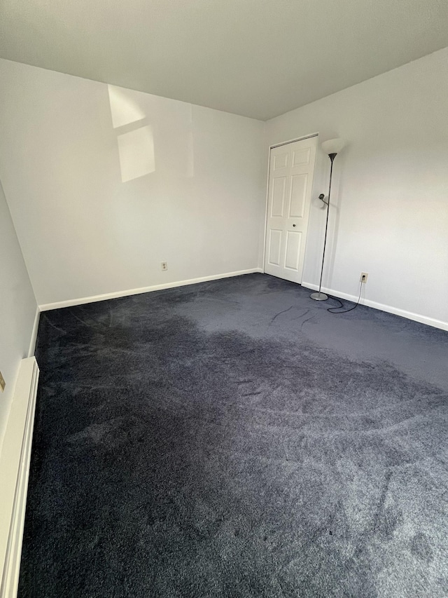 empty room with baseboard heating and dark carpet