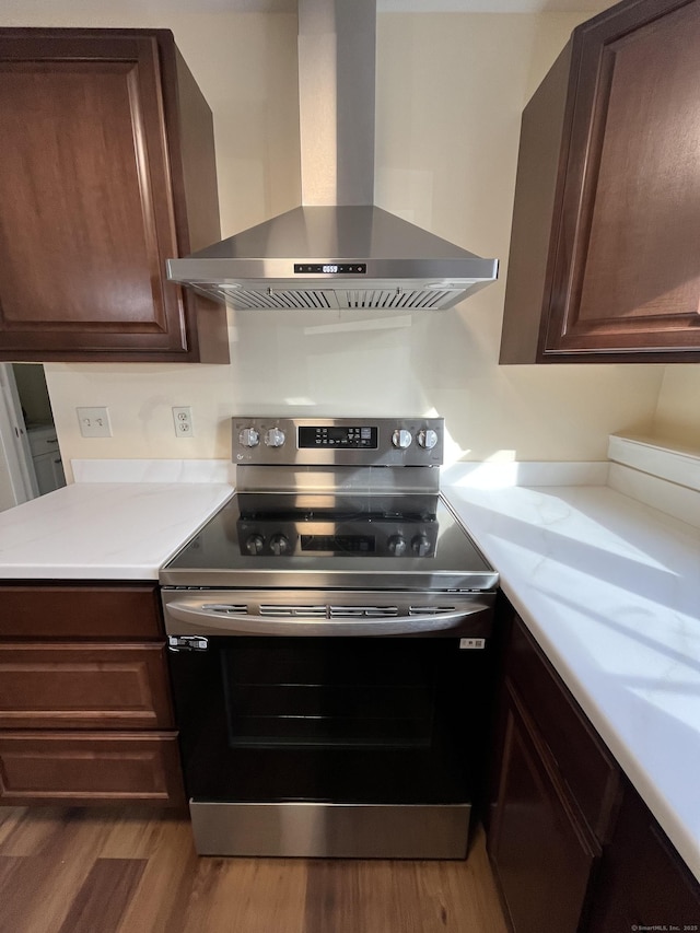 kitchen with electric range, dark brown cabinets, hardwood / wood-style floors, and wall chimney range hood