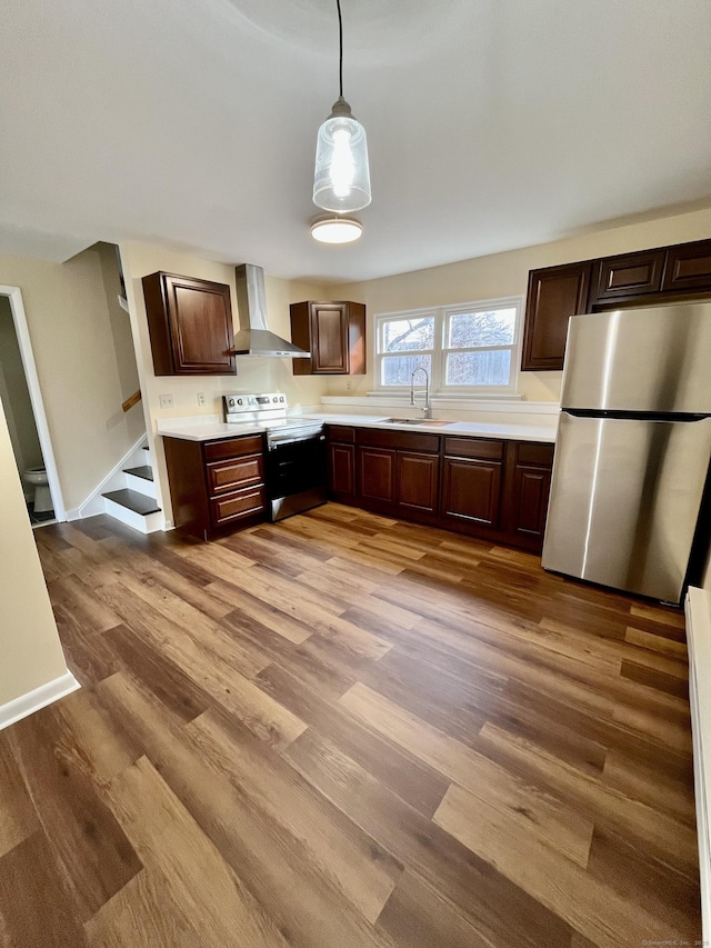 kitchen with sink, wall chimney exhaust hood, pendant lighting, wood-type flooring, and appliances with stainless steel finishes