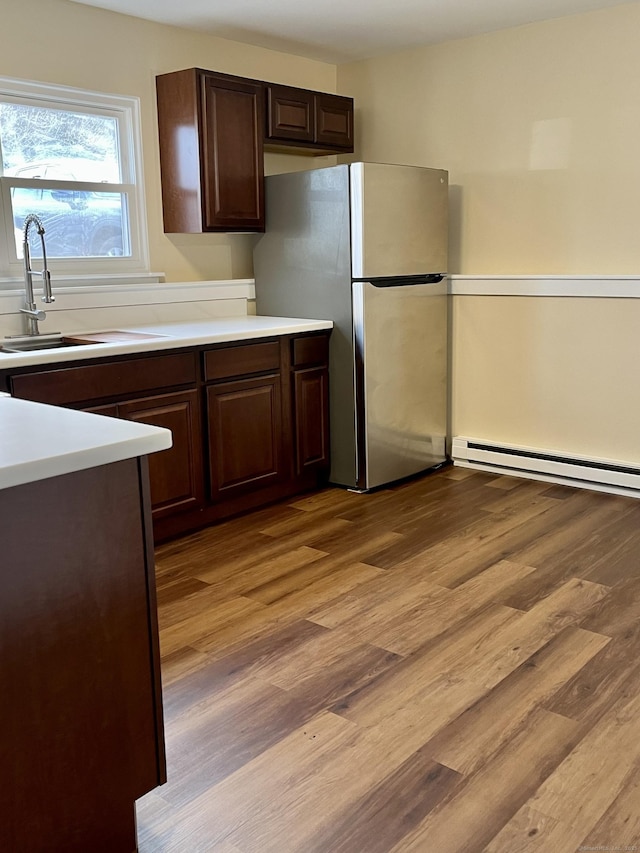 kitchen featuring dark brown cabinetry, sink, a baseboard radiator, light hardwood / wood-style floors, and stainless steel refrigerator