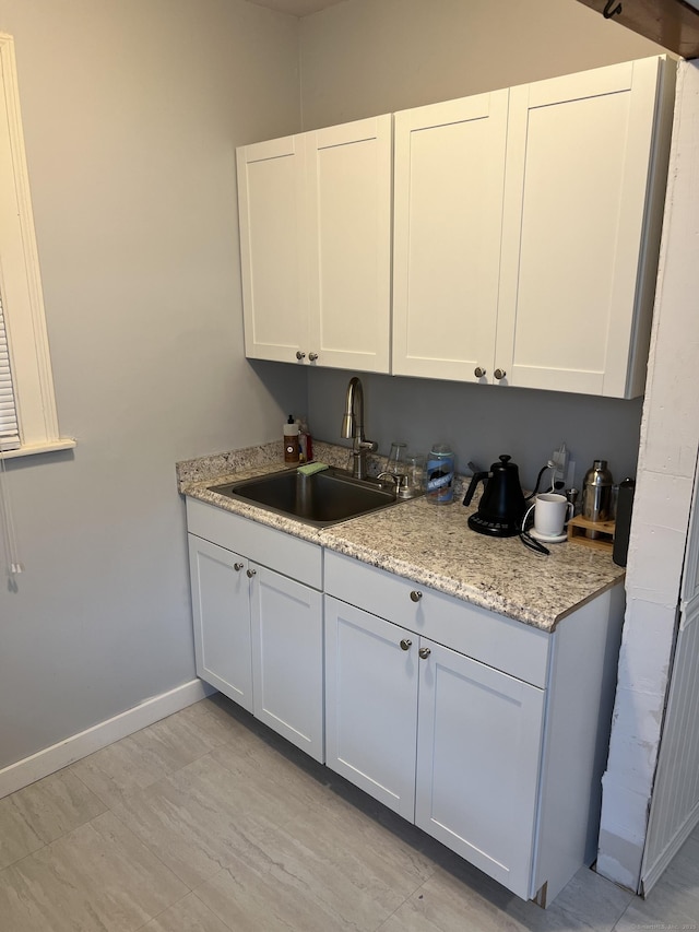 kitchen with white cabinets, light stone counters, and sink