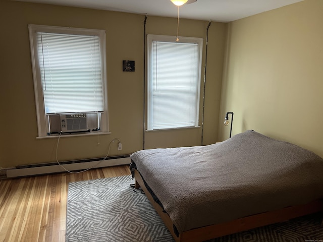 bedroom with multiple windows, hardwood / wood-style flooring, cooling unit, and a baseboard heating unit