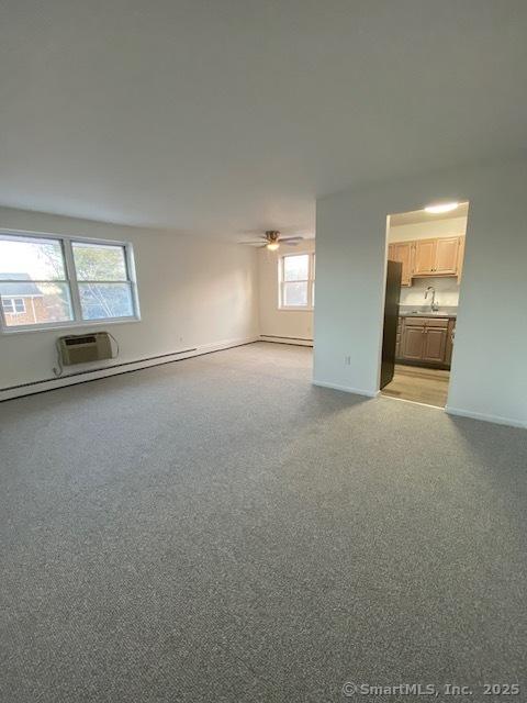 carpeted empty room featuring a baseboard radiator, a wall unit AC, and ceiling fan