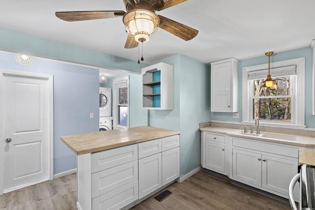 kitchen featuring wood counters, stacked washer / drying machine, decorative light fixtures, white cabinets, and sink