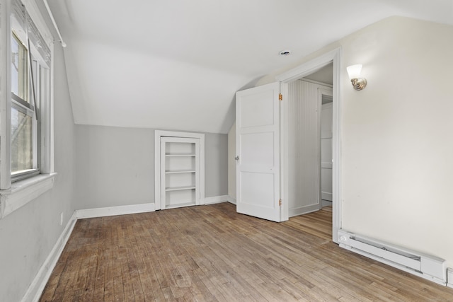 bonus room with a baseboard heating unit, built in features, lofted ceiling, and light wood-type flooring