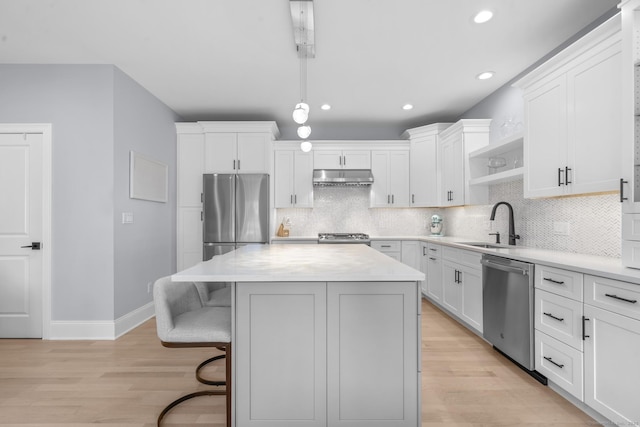 kitchen with appliances with stainless steel finishes, backsplash, sink, white cabinets, and a center island