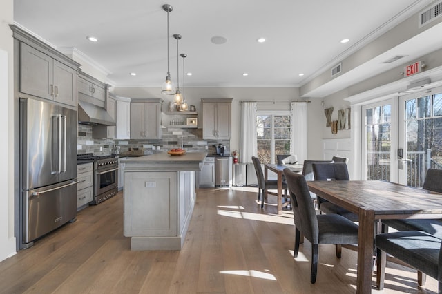 kitchen with decorative light fixtures, high quality appliances, gray cabinets, a kitchen island, and range hood