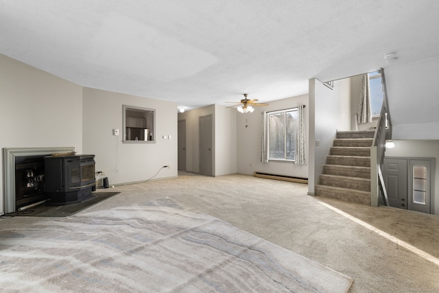 unfurnished living room featuring ceiling fan, a wood stove, a baseboard heating unit, and plenty of natural light