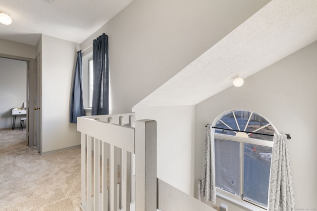 hall with light carpet, vaulted ceiling, and a textured ceiling