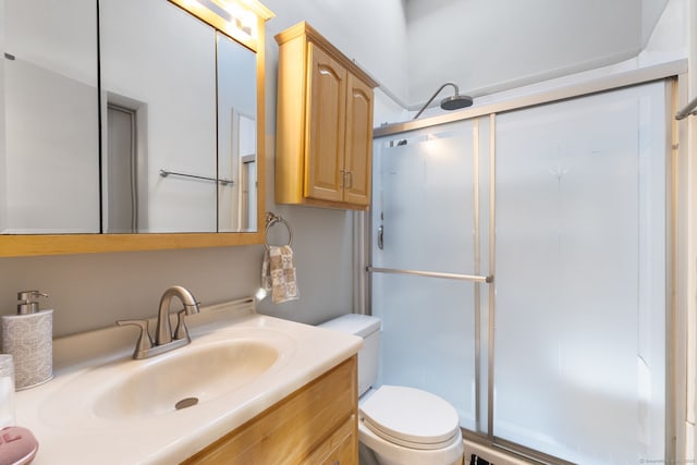 bathroom featuring toilet, vanity, and a shower with door