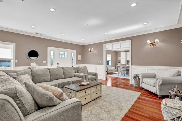 living area with visible vents, crown molding, light wood-style floors, and a wainscoted wall