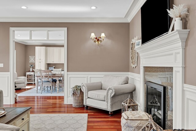 living area with crown molding, wood finished floors, a wainscoted wall, and a high end fireplace