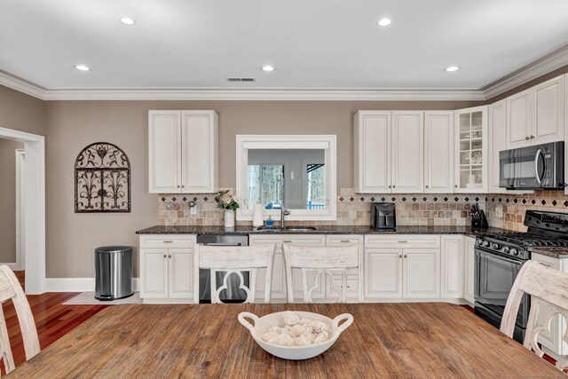 kitchen featuring glass insert cabinets, crown molding, light wood-type flooring, black appliances, and a sink