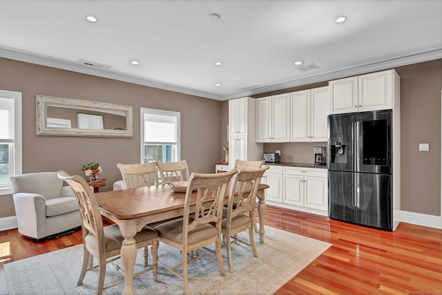 dining room featuring baseboards, visible vents, light wood finished floors, and ornamental molding