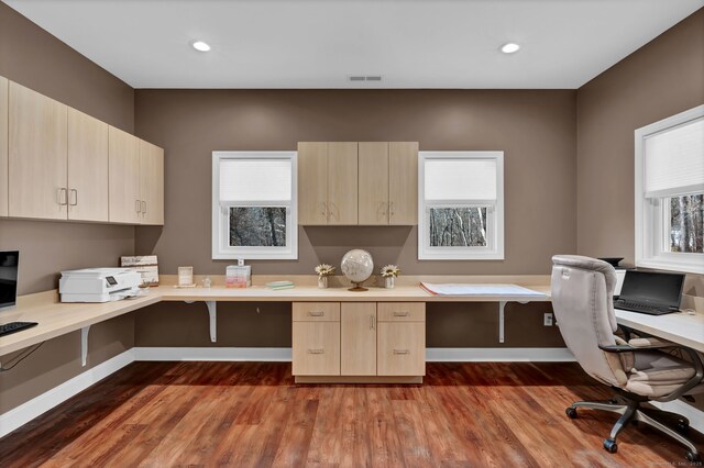 office area with dark wood finished floors, plenty of natural light, visible vents, and built in desk