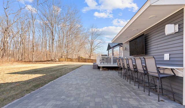 view of patio with outdoor dry bar, a deck, and fence