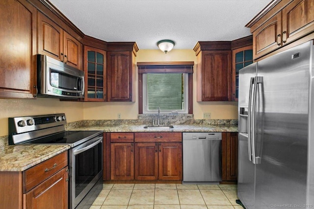 kitchen with sink, light tile patterned floors, a textured ceiling, light stone countertops, and appliances with stainless steel finishes