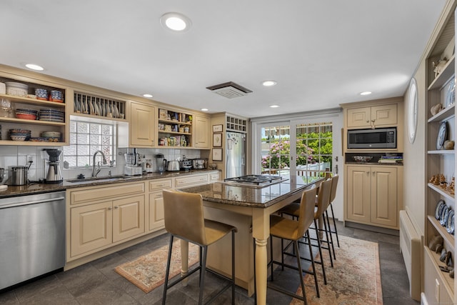 kitchen with a kitchen breakfast bar, sink, dark stone countertops, a kitchen island, and stainless steel appliances