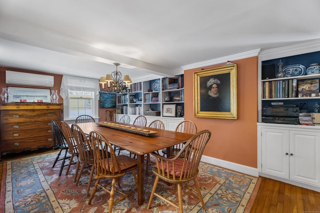 dining room featuring built in features, a wall mounted AC, hardwood / wood-style floors, a chandelier, and ornamental molding