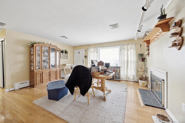 living room featuring baseboard heating, a tile fireplace, light hardwood / wood-style flooring, and rail lighting