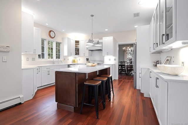 kitchen with a kitchen island, baseboard heating, dark hardwood / wood-style floors, a kitchen bar, and white cabinets