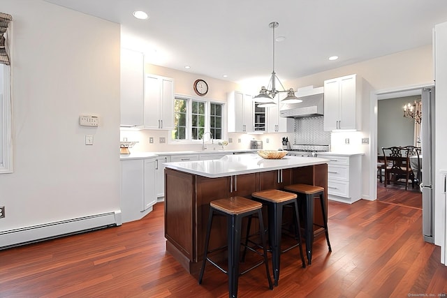 kitchen featuring dark hardwood / wood-style flooring, wall chimney range hood, white cabinets, a chandelier, and a kitchen island