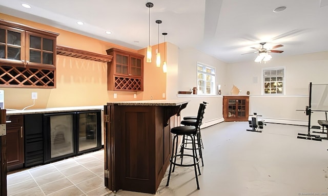 bar featuring dark brown cabinets, baseboard heating, ceiling fan, wine cooler, and hanging light fixtures