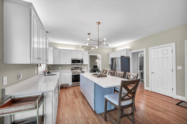 kitchen featuring stainless steel appliances, sink, white cabinets, a kitchen island, and hanging light fixtures