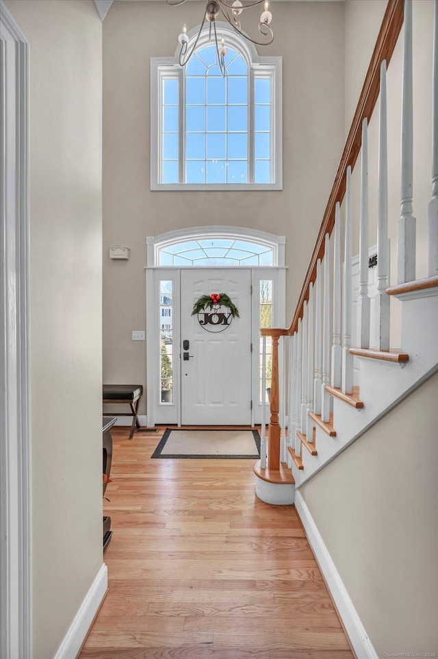 foyer entrance with light wood-type flooring, a towering ceiling, and an inviting chandelier