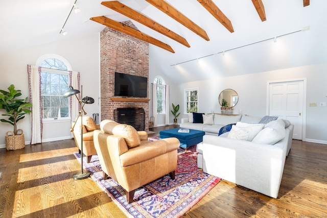 living room featuring dark wood-type flooring, rail lighting, a brick fireplace, and vaulted ceiling with beams