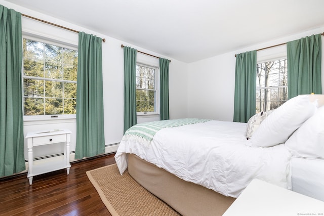 bedroom with dark wood-type flooring, baseboard heating, and multiple windows