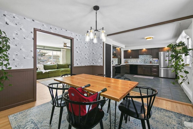 dining room with light wood-type flooring, ceiling fan with notable chandelier, and beam ceiling