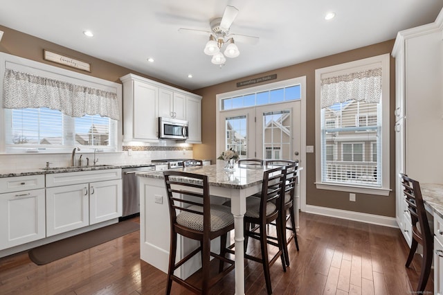 kitchen with light stone counters, stainless steel appliances, sink, white cabinets, and a center island