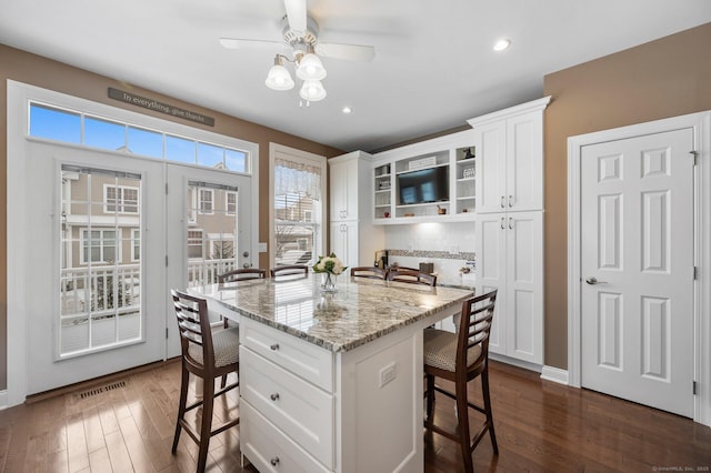 kitchen featuring white cabinets, a kitchen breakfast bar, a kitchen island, and light stone countertops