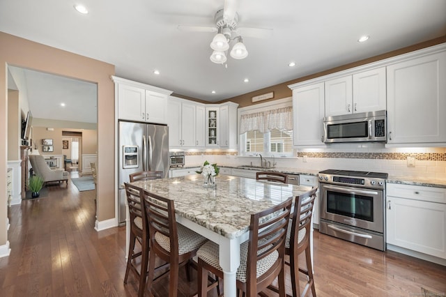 kitchen with stainless steel appliances, white cabinetry, dark wood-type flooring, and light stone counters